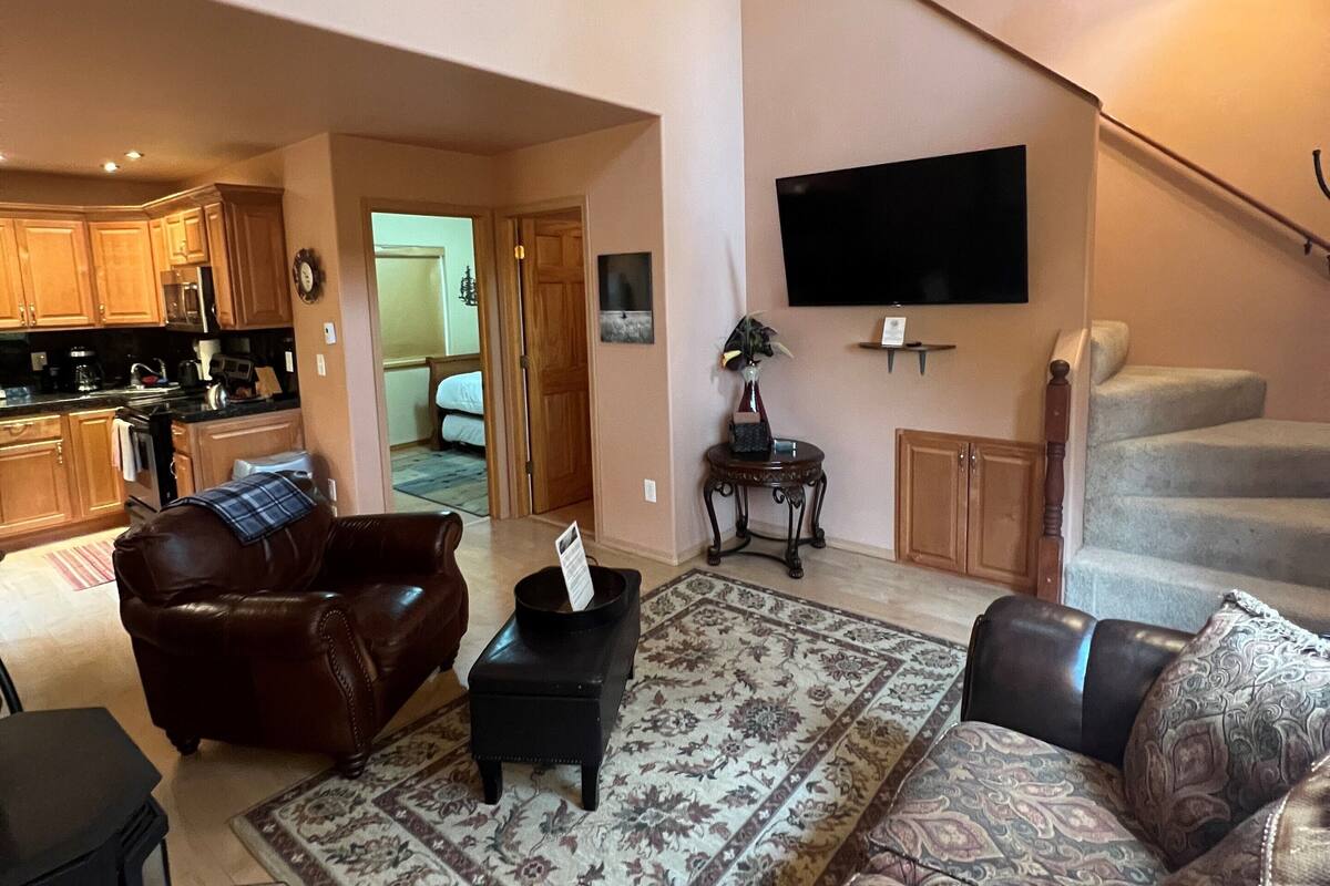 A spacious living room with a large rug, leather sofas, a flat-screen TV, and a mounted animal hide.