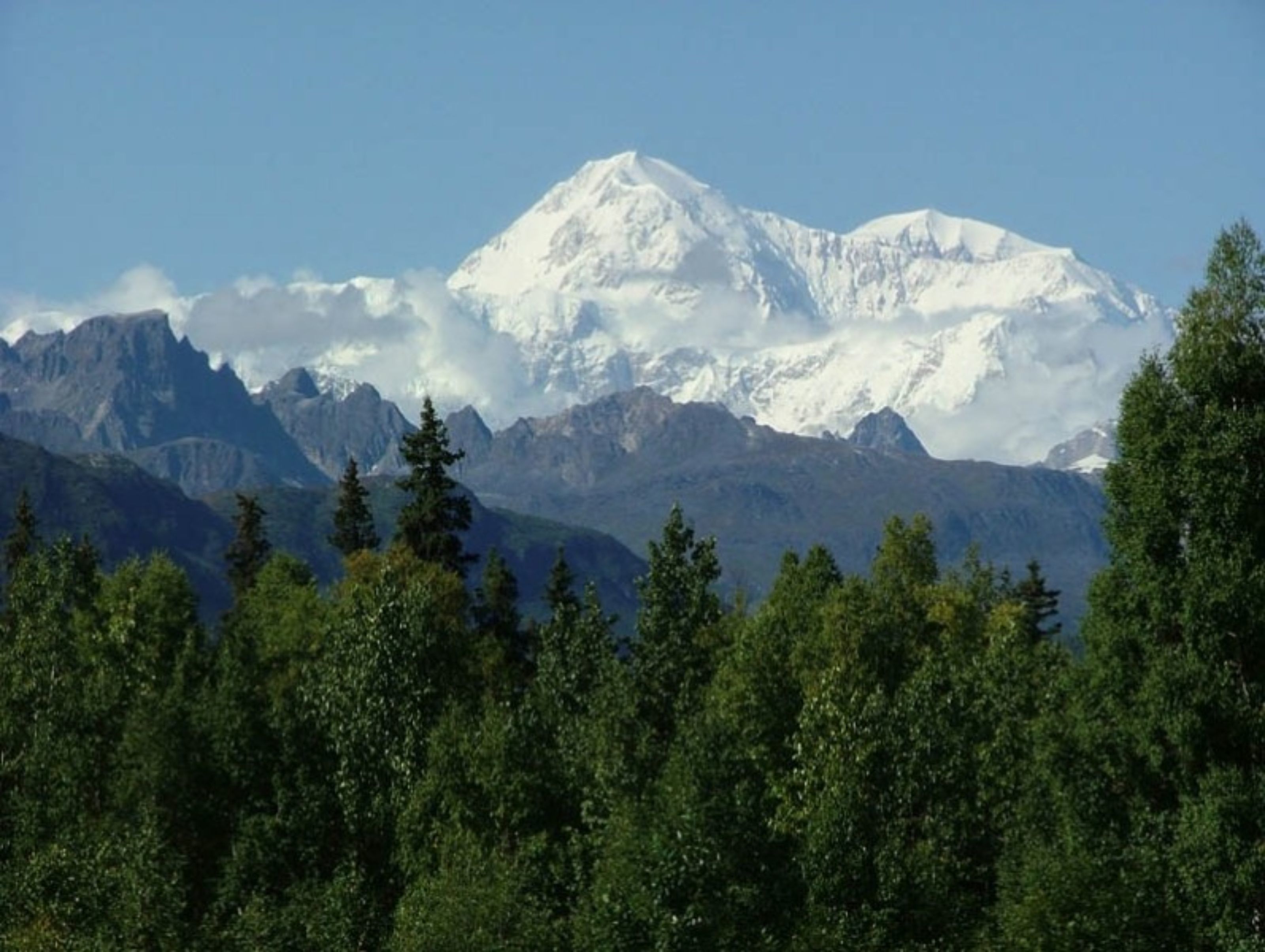 A mountain landscape with a prominent snow-capped peak and dense forest in the foreground.