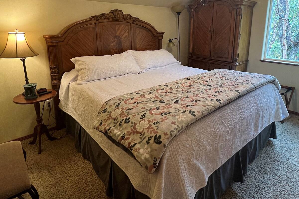A neatly made bed with a floral bedspread, a wooden headboard, a nightstand with a lamp, and a wardrobe.
