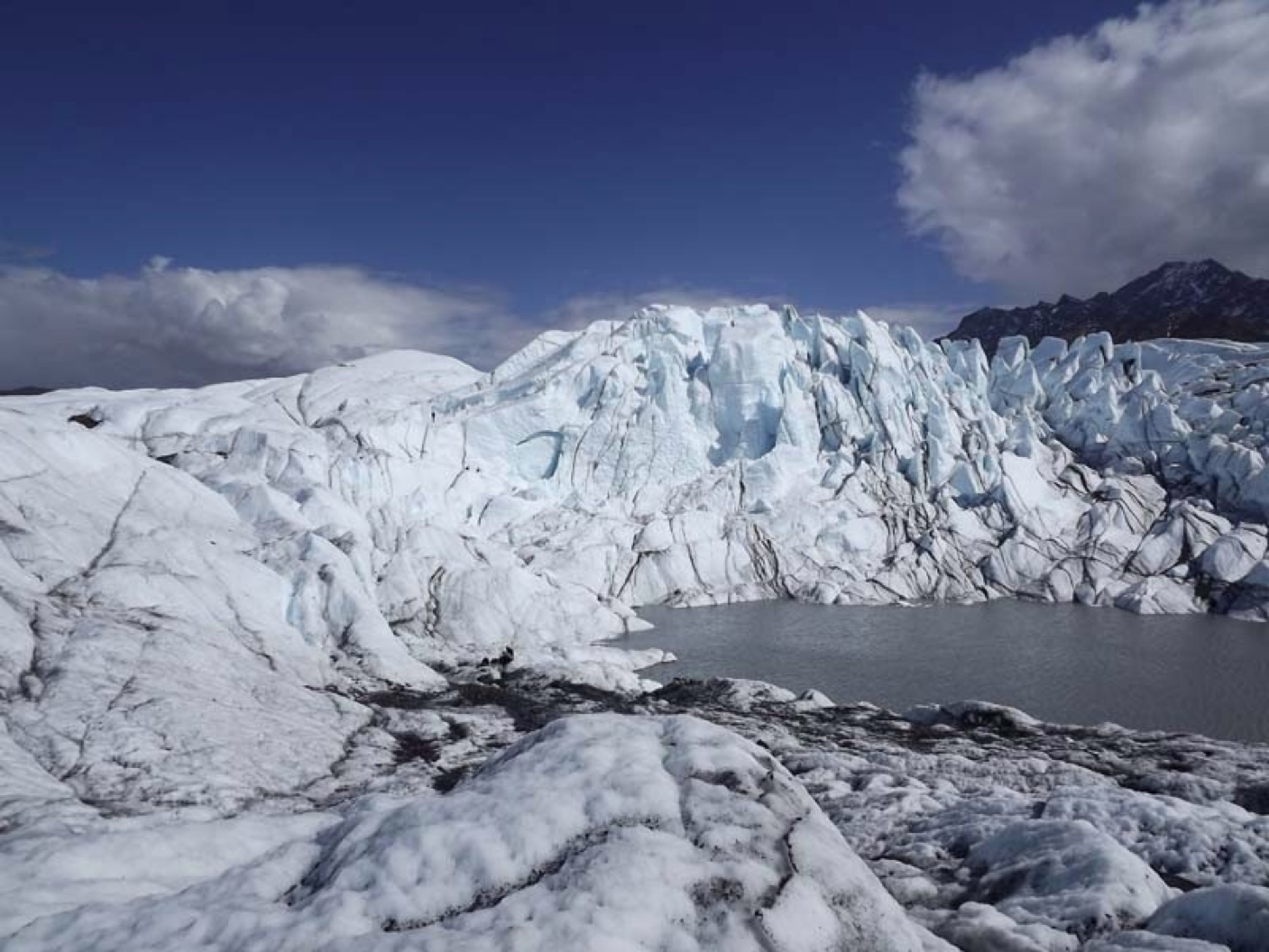 A glacier with a lake and mountains in the background.