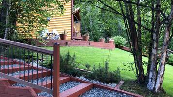 A wooden cabin with a red staircase leading to a deck, surrounded by a well-maintained lawn and trees.