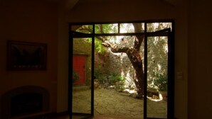 A room with a fireplace, a framed picture on the wall, and a large sliding glass door leading to an outdoor area with a stone wall and a tree.
