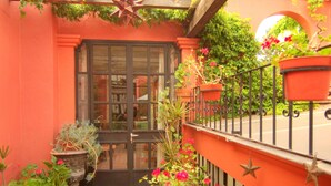 A red building with a black door, potted plants, and a metal railing.