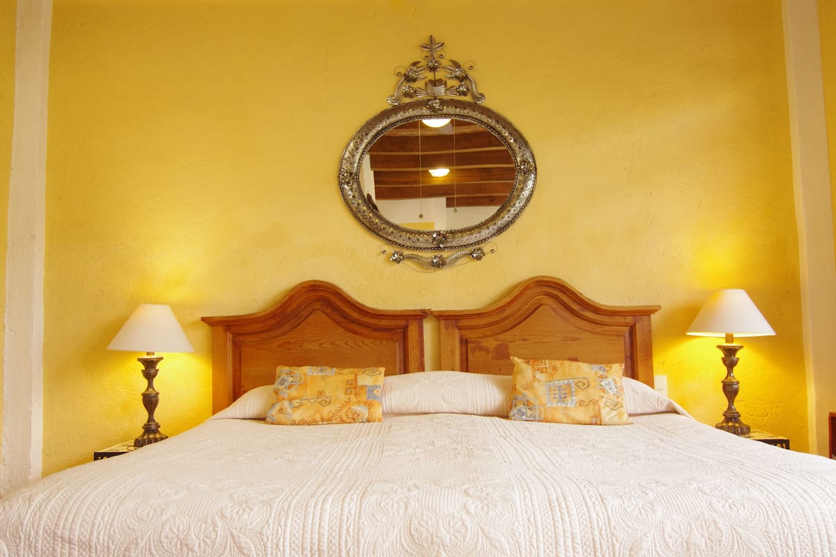 Una cama con cabecera de madera, dos lámparas de noche y almohadas estampadas.