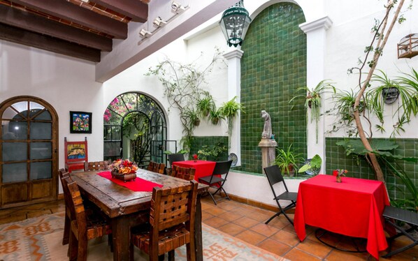 Un patio con mesas y sillas de madera, una estatua y plantas en macetas.