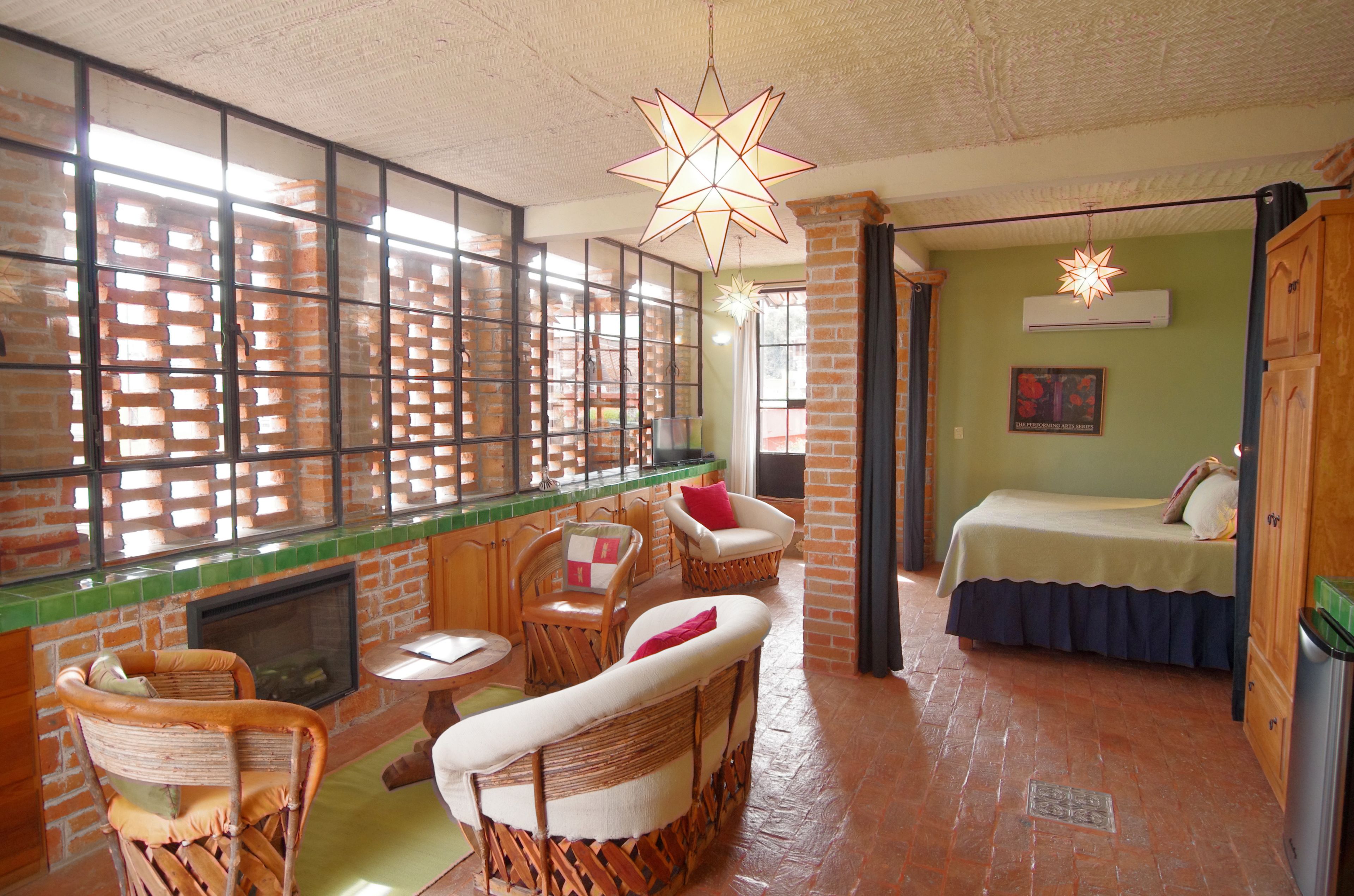 A room with a brick fireplace, wicker furniture, a bed with a blue bedspread, and a star-shaped hanging light fixture.