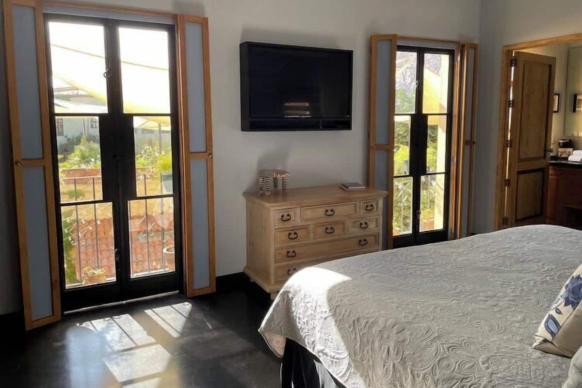 Un dormitorio con cama, cómoda, televisor y ventanas amplias con vistas al exterior.