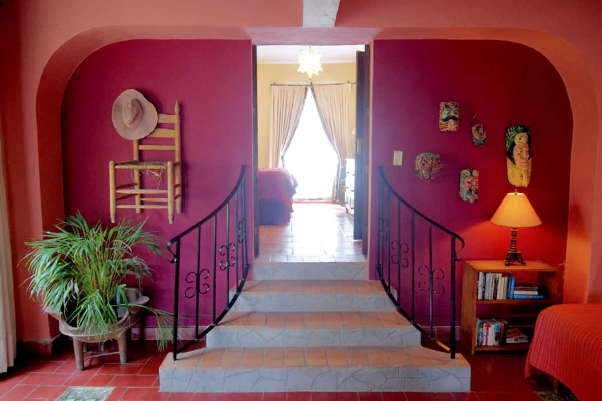 Una escalera con barandilla de madera, una planta en maceta y una estantería con libros.