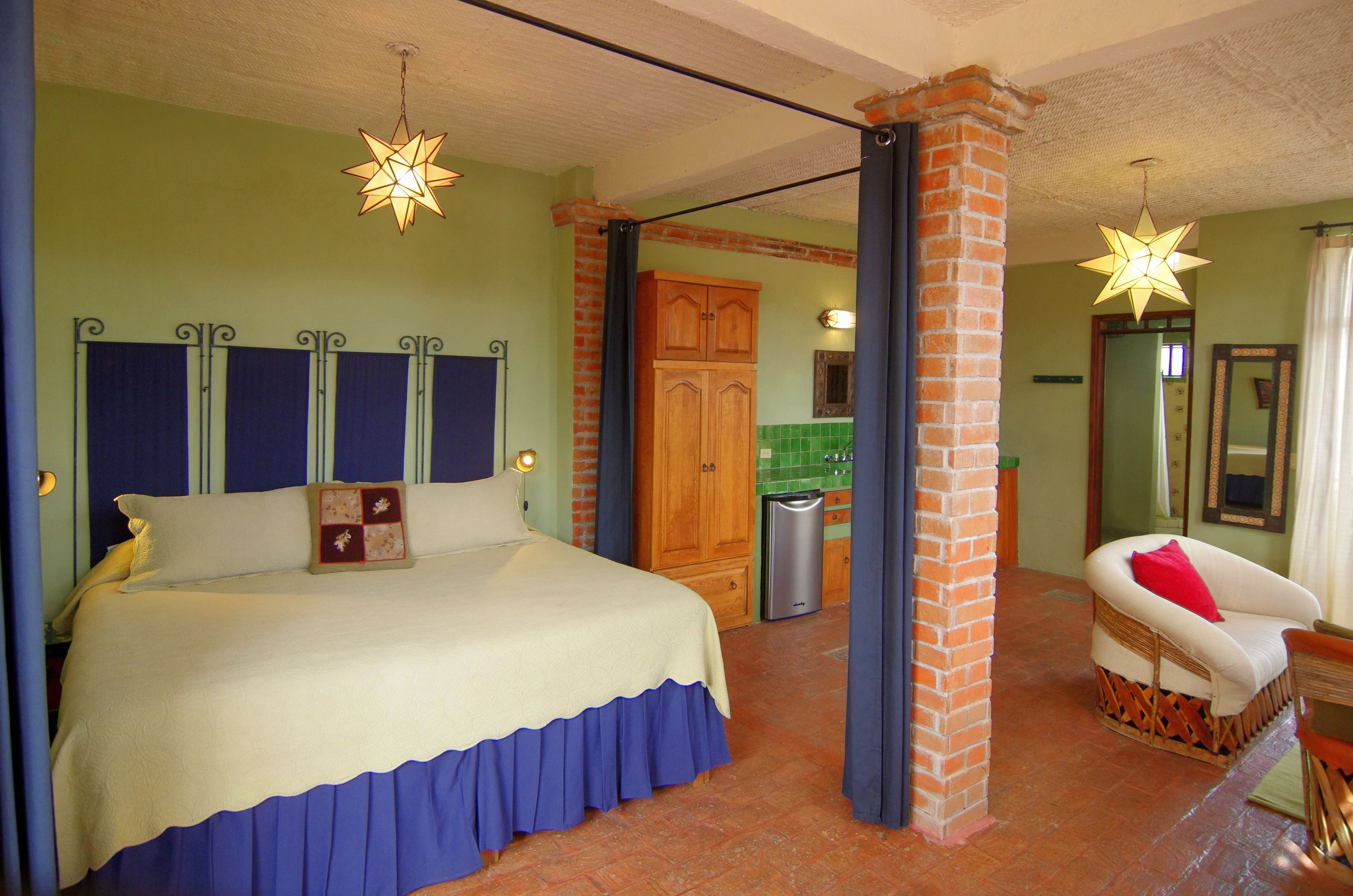 Un dormitorio con una cama grande, un aparador de madera, una silla de mimbre y una lámpara colgante en forma de estrella.