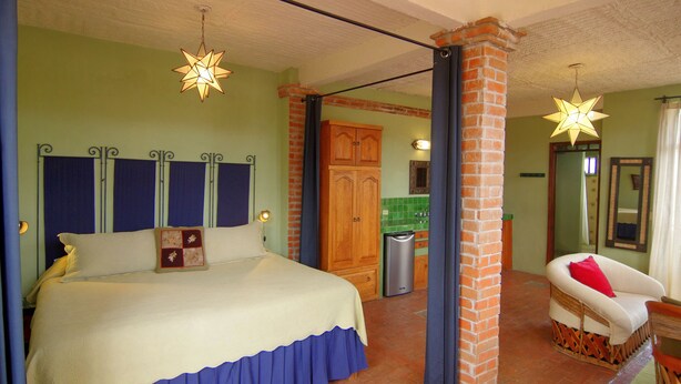 A bedroom with a large bed, a wooden cabinet, a wicker chair, and a star-shaped hanging light. - Casa de la Noche (San Miguel de Allende)