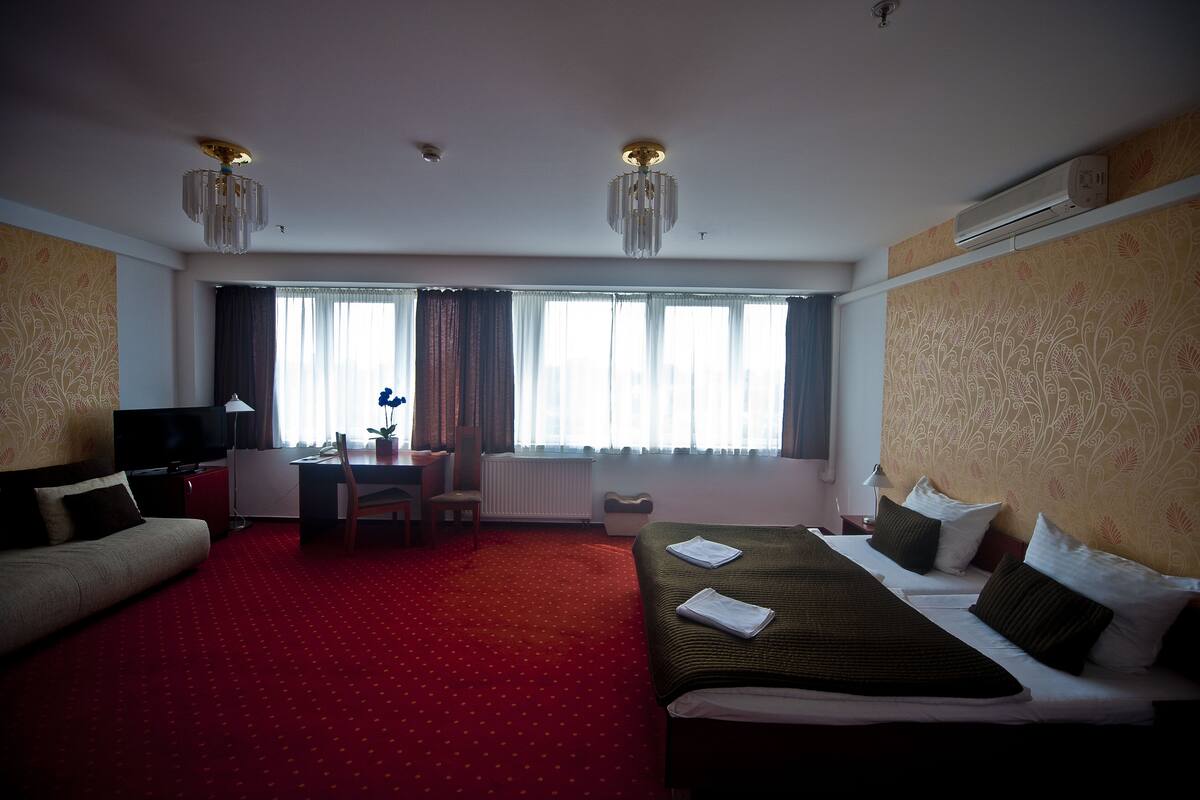 Una habitación de hotel con dos camas, un escritorio, un televisor y un ventanal grande con cortinas.