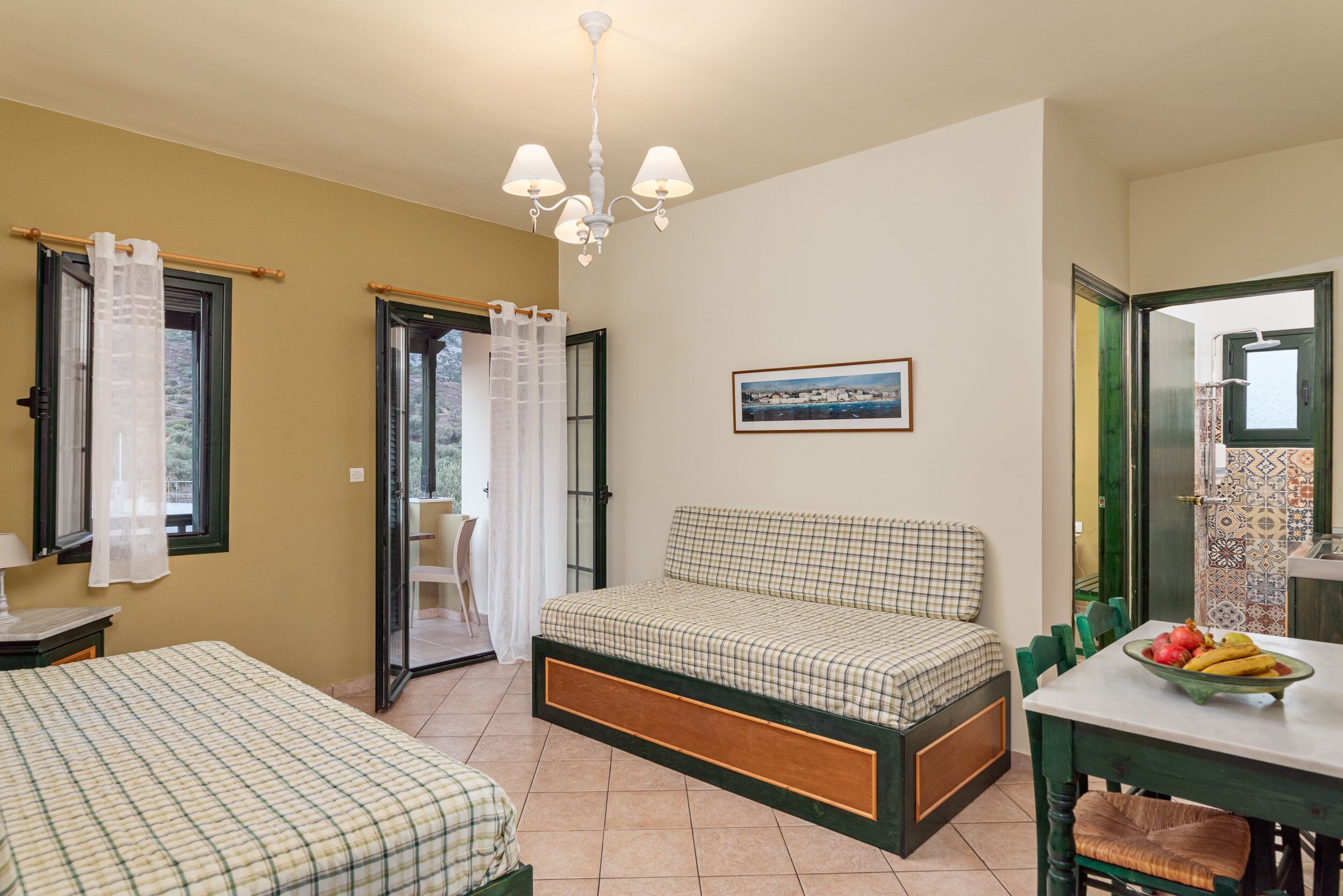 A room with two beds, a dining table with fruit, a chandelier, and a painting on the wall.