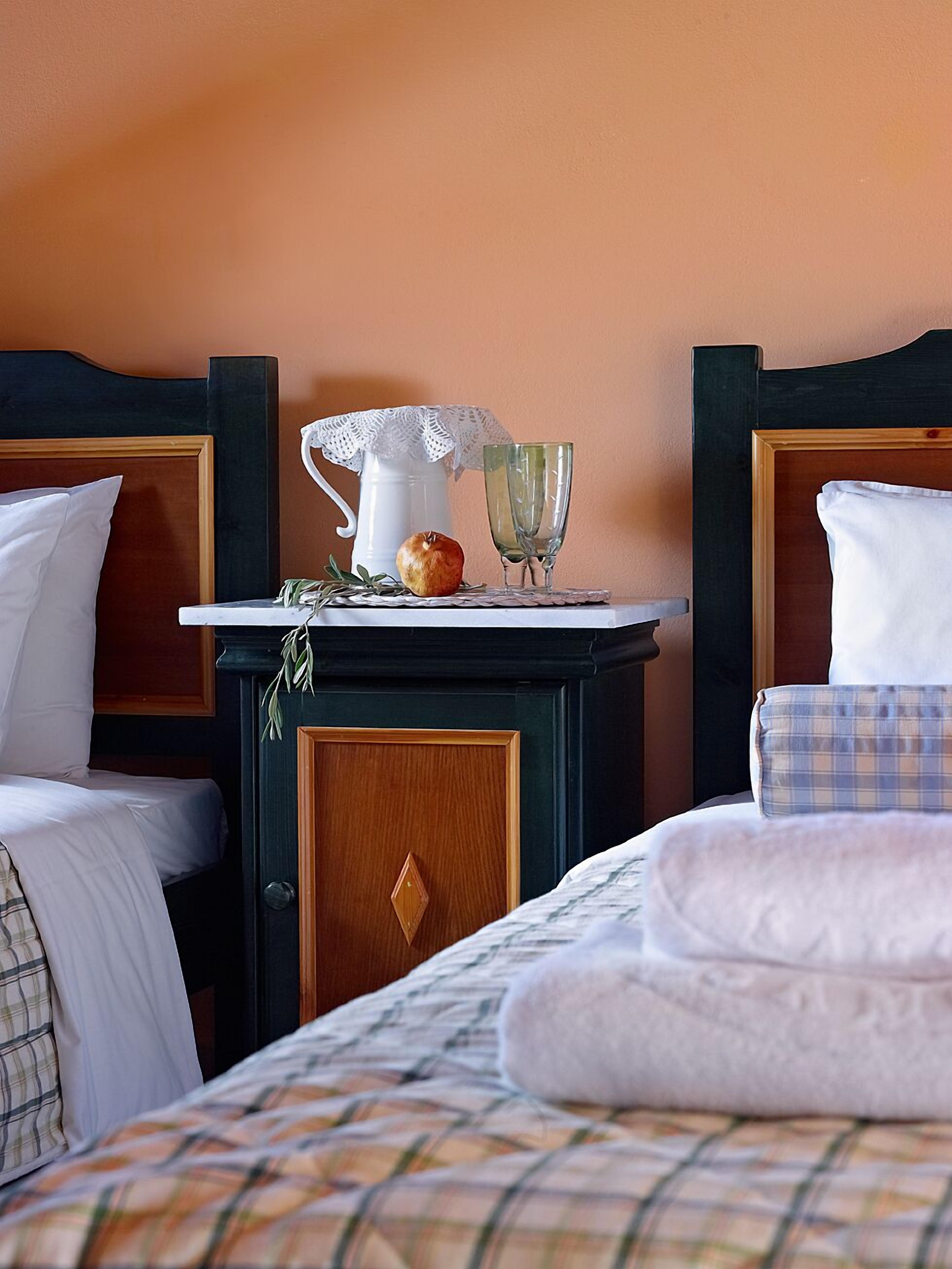 Una camera d'albergo con due letti, un comodino con una caraffa, un bicchiere e una mela.