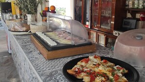 A buffet setup with a variety of food items, including a large plate of pizza, a glass display case with pastries, and a buffet counter with utensils and condiments.