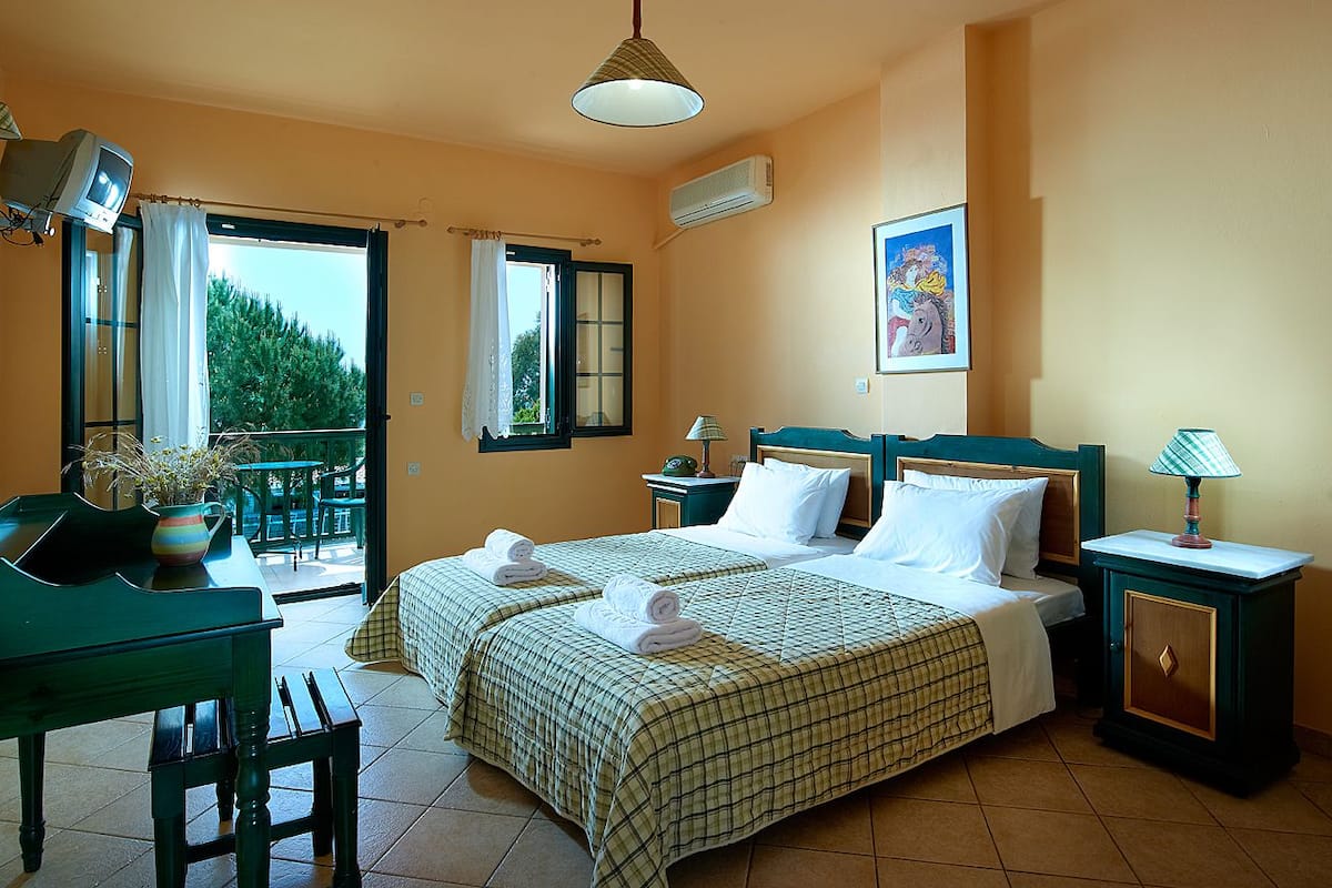 A hotel room with two beds, a balcony, a desk, and a chair.