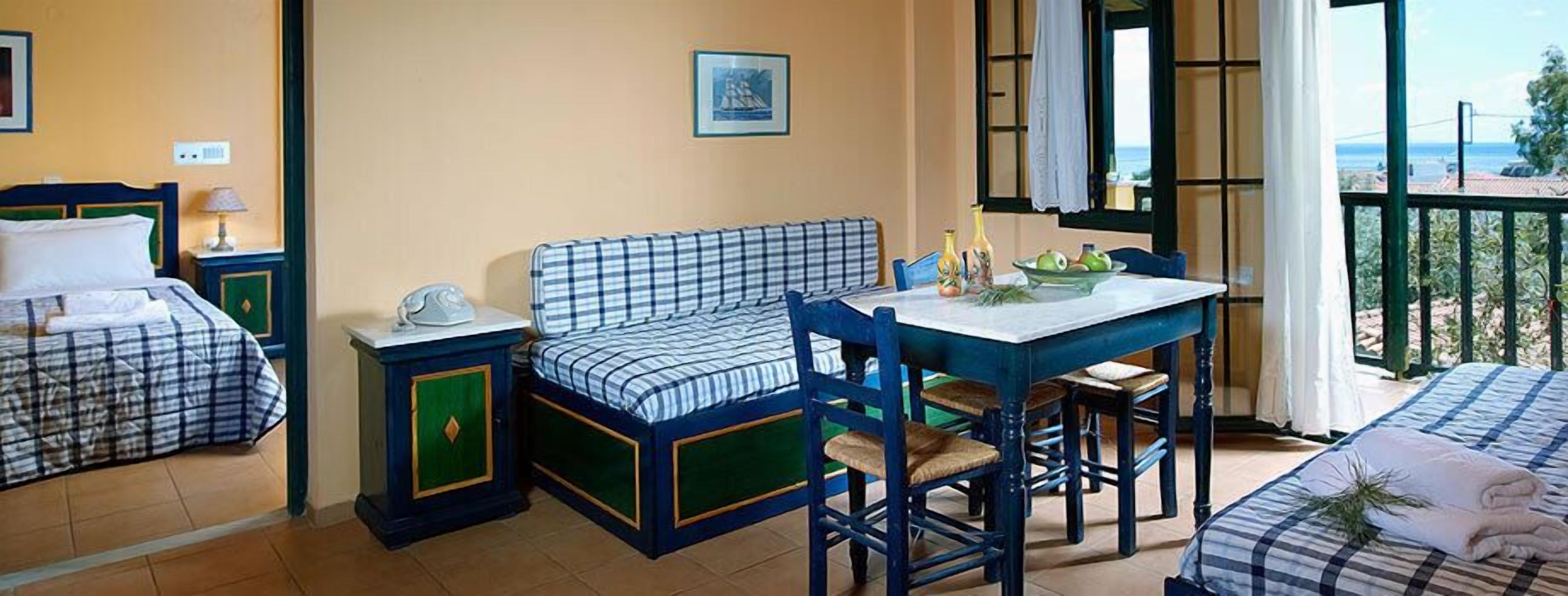 A room with two beds, a dining table, and a balcony with a view.