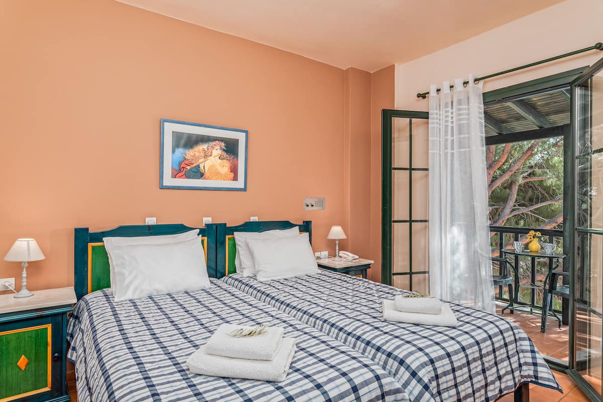 A bedroom with a bed, two bedside tables, a nightstand, a window with a view, and a painting on the wall.
