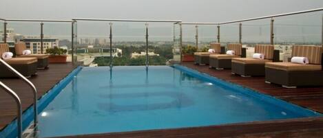 Una piscina infinita en la azotea con sillones de descanso y plantas en macetas.