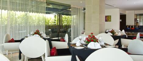 A dining area with tables set for a meal, featuring white chairs and black tablecloths.