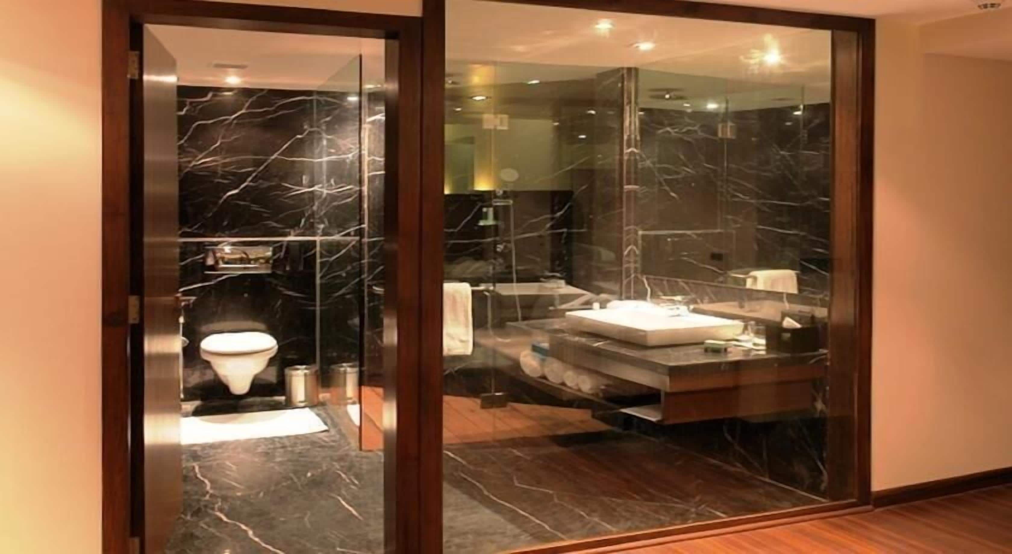 Ein modernes Badezimmer mit Glastrennwand, Marmorboden und sichtbarer Toilette.