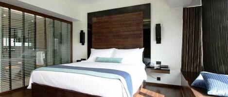 A modern hotel room with a large bed, wooden flooring, a dark headboard, and a view through floor-to-ceiling windows.