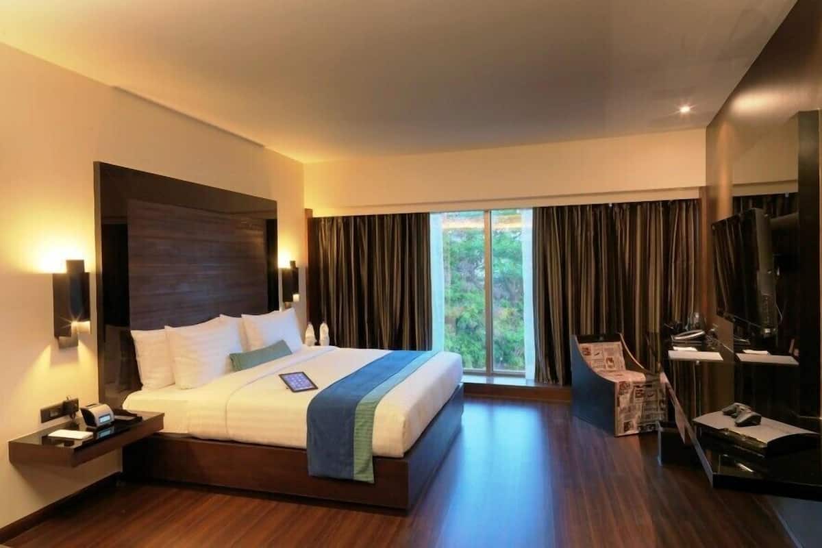 Ein modernes Hotelzimmer mit einem großen Bett, einem Schreibtisch mit Computer, einem Fernseher und einem Fenster mit Vorhängen.
