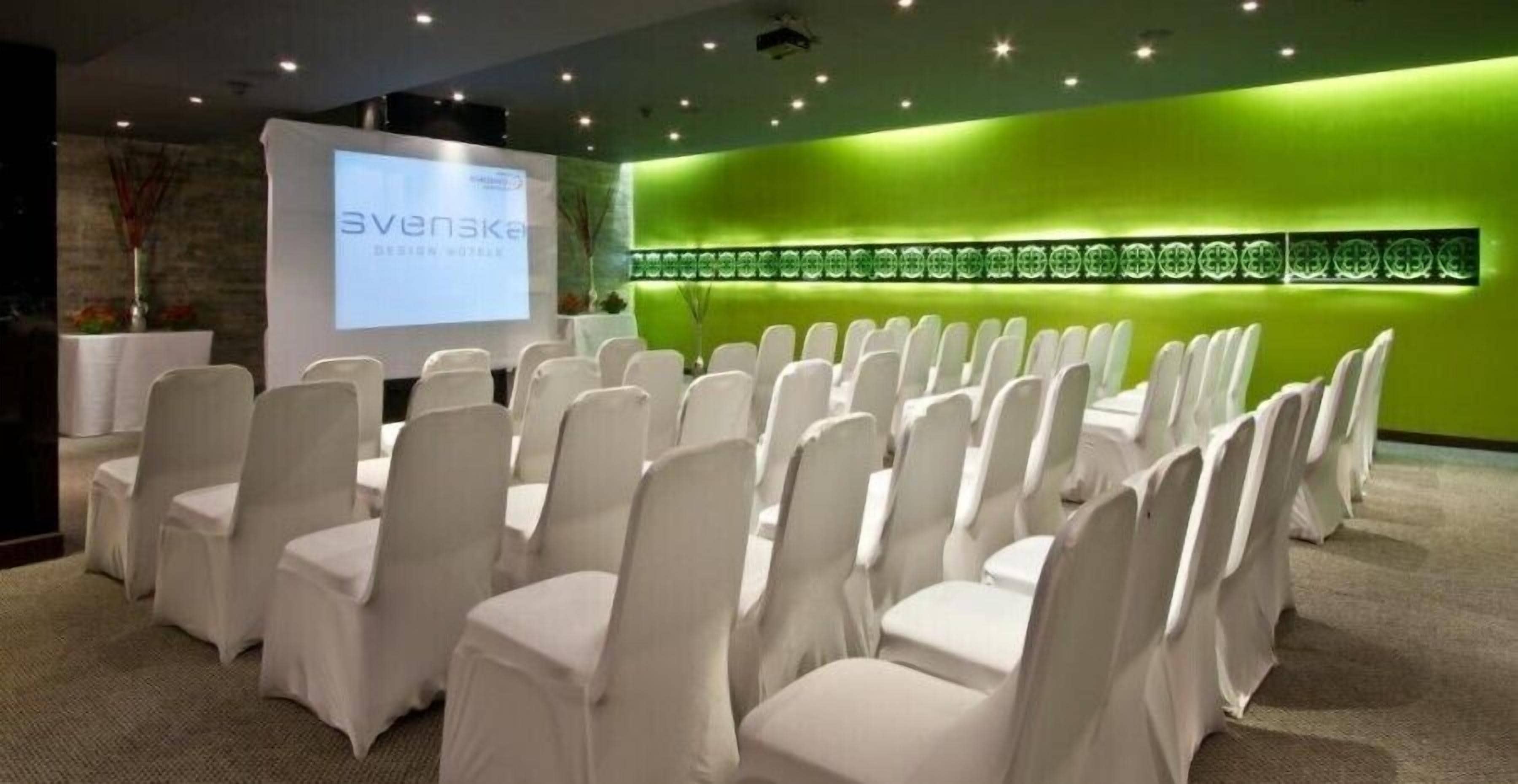 A conference room with rows of white chairs and a presentation screen.