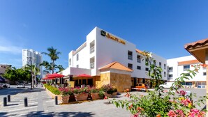 Un hotel con fachada blanca, un letrero que dice "Quality Inn", y mobiliario exterior con sombrillas rojas.