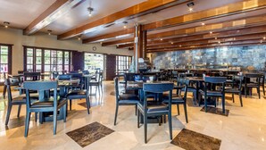 Un vaste espace dédié à la salle à manger, avec de nombreuses tables et chaises, un mur en pierre et de grandes fenêtres.