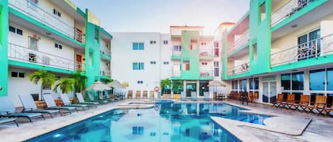 Un hotel con piscina central, varios balcones y zonas de estar al aire libre.