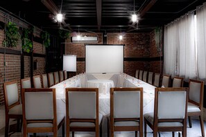 A conference room with a long table, chairs, a projector screen, and a brick wall. - Quality Inn Mazatlan (Mazatlán)