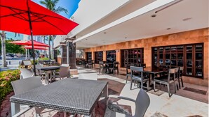 Un espace café en plein air avec des tables et des chaises, des parasols rouges et une vue sur la rue.