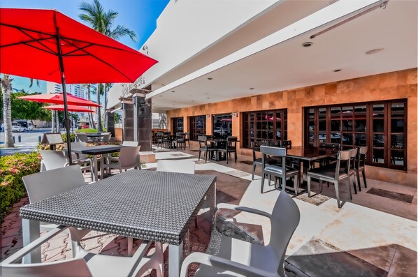 An outdoor cafe area with tables and chairs, red umbrellas, and a view of the street. - Quality Inn Mazatlan (Mazatlán)