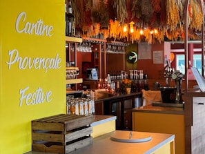 A bar area with shelves of bottles and glasses, a wooden crate, and a yellow wall with text.