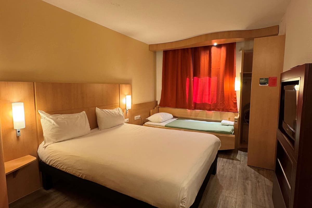 A hotel room with a large bed, a bedside table, a TV, and a window with curtains.