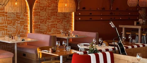 Interior de restaurante con cabinas, mesas y lámparas colgantes.
