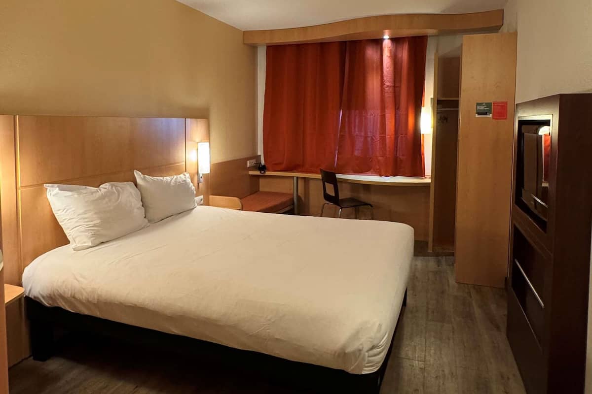 A hotel room with a bed, desk, chair, and a television.