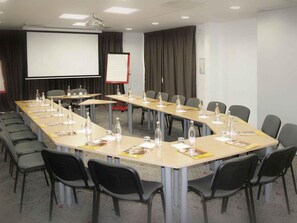 Une salle de conférence équipée d’une longue table, de chaises, d’un écran de projection et d’un tableau blanc.