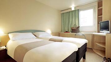 A hotel room with two beds, a desk, a television, and a window with curtains.