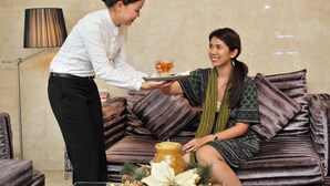 A person serving a drink to another person seated on a sofa with patterned cushions. - Sanouva Saigon Hotel (Ho Chi Minh City)