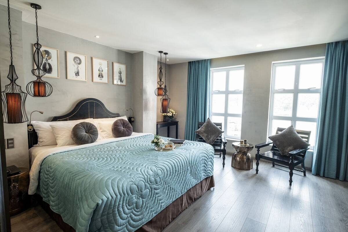 Une chambre à coucher avec un grand lit, une chaise en bois, une petite table et une fenêtre avec des rideaux.