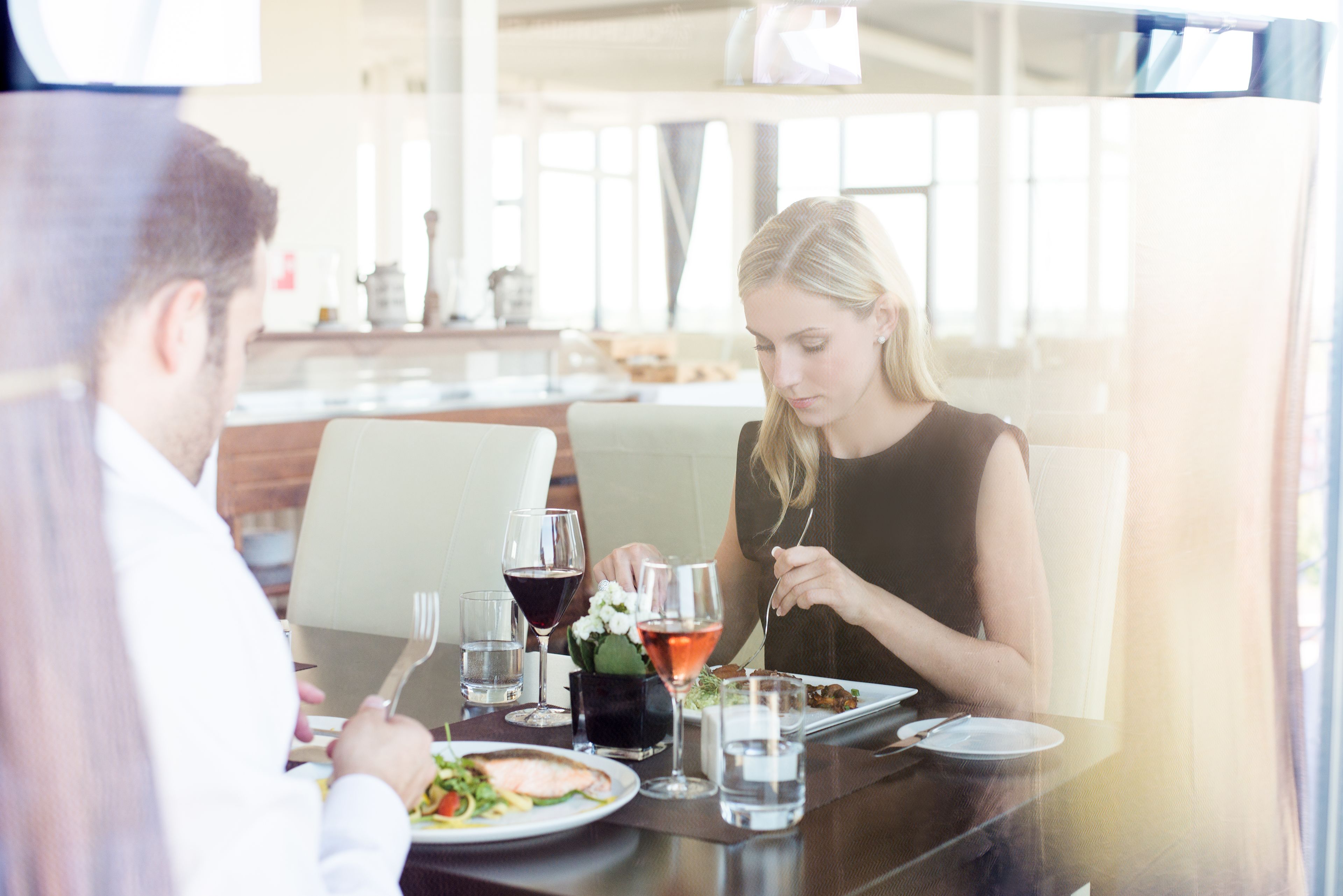 A dining table with plates of food, glasses of water and wine, and a vase of flowers.