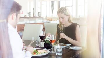 A dining table with plates of food, glasses of water and wine, and a vase of flowers.