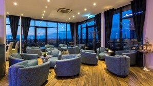 Un moderno espacio de descanso con varias opciones de asientos, amplios ventanales que ofrecen vistas a la ciudad y suelo de madera.