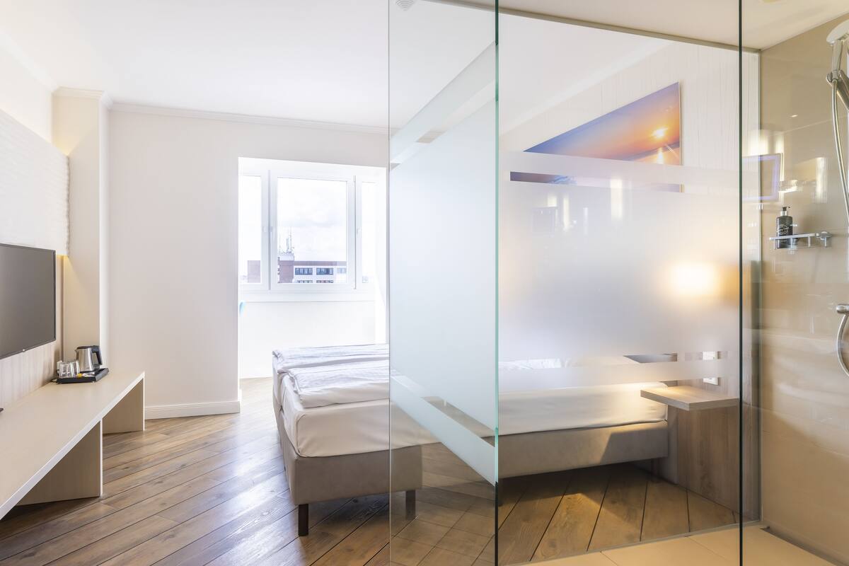 Habitación de hotel moderna con un separador de vidrio que divide la zona de estar y el baño.