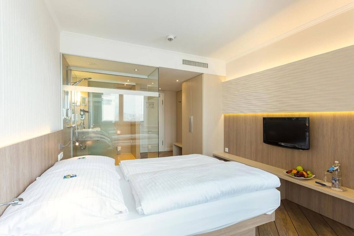Una habitación de hotel con una cama, televisión, espejo y una pequeña mesa con fruta.