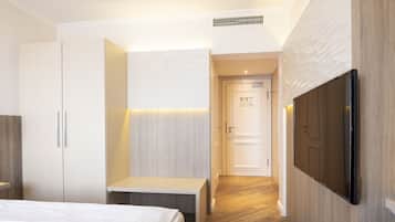 A hotel room with a bed, a bench, a wardrobe, a television, and a door leading to another room.