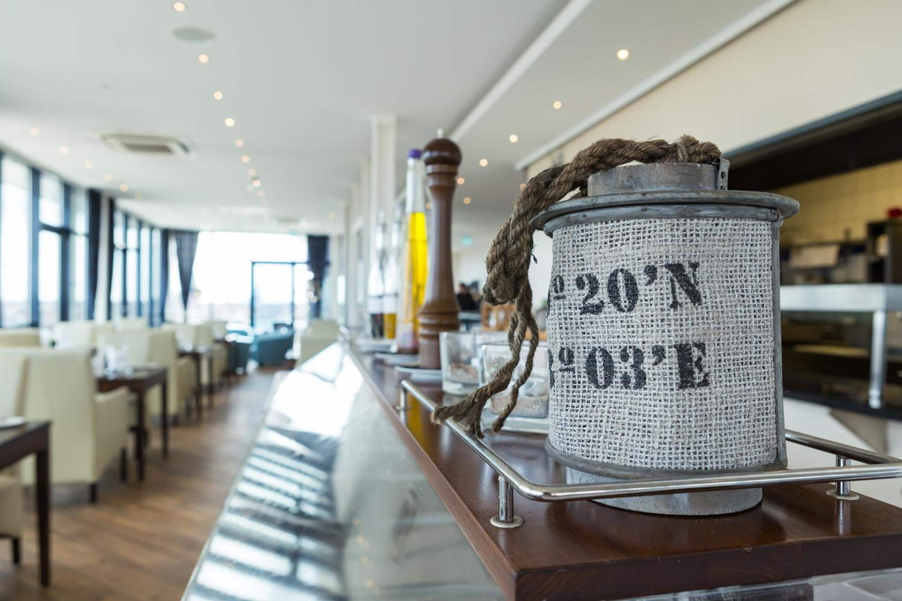 Una zona de bar con un recipiente de aspecto rústico que lleva la etiqueta "20'N 03'E" sobre una barra de madera.