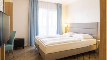 A hotel room with a large bed, a TV, a small table, and a window with curtains.