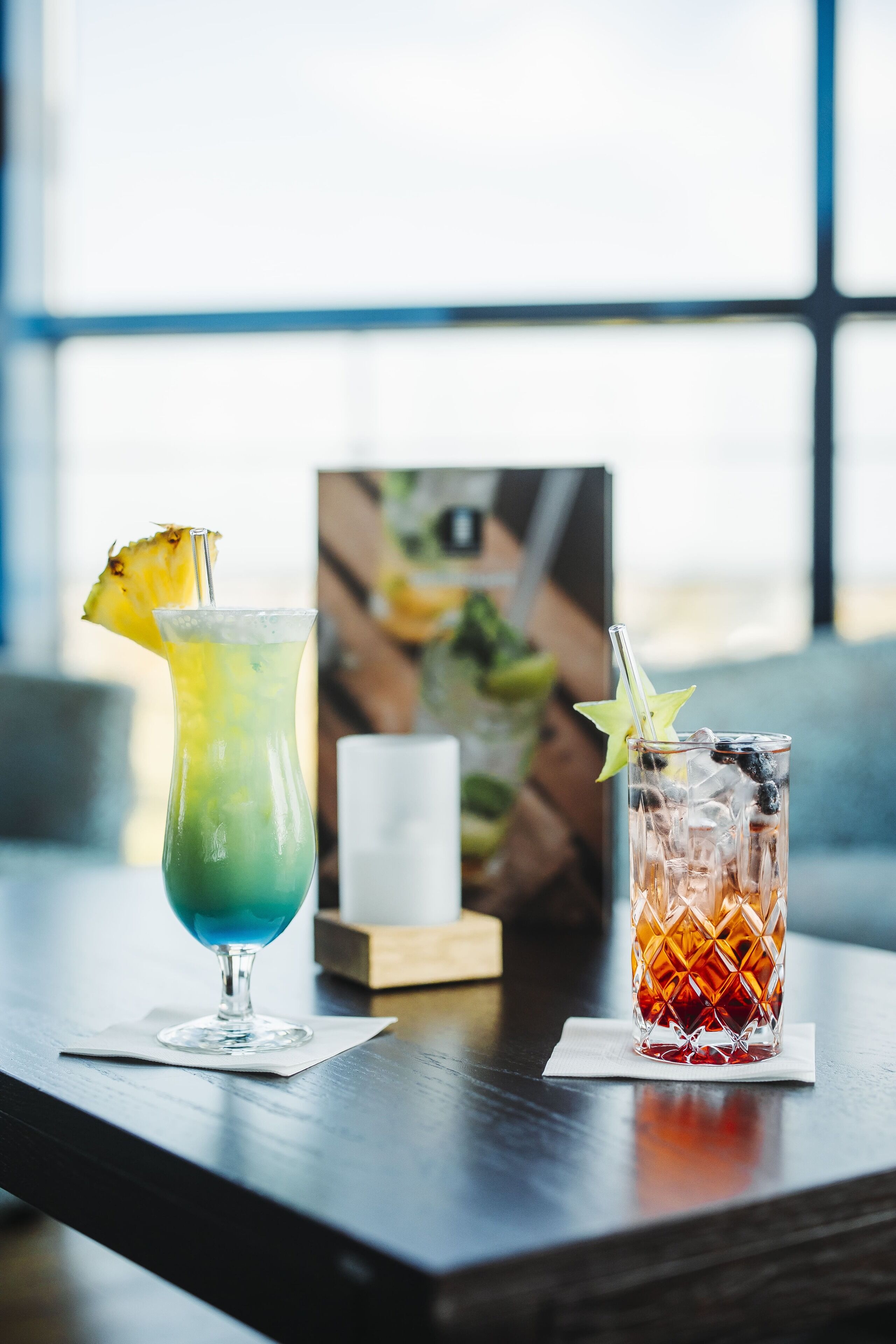 Two cocktails on a wooden table with a framed picture in the background.